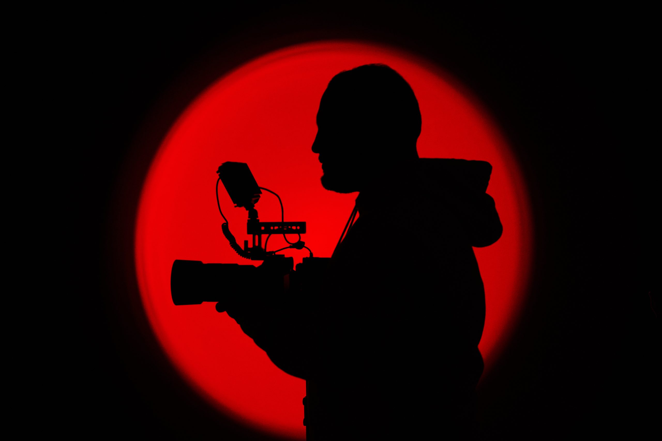 Cinematographer silhouetted against a red light, holding a camera rig